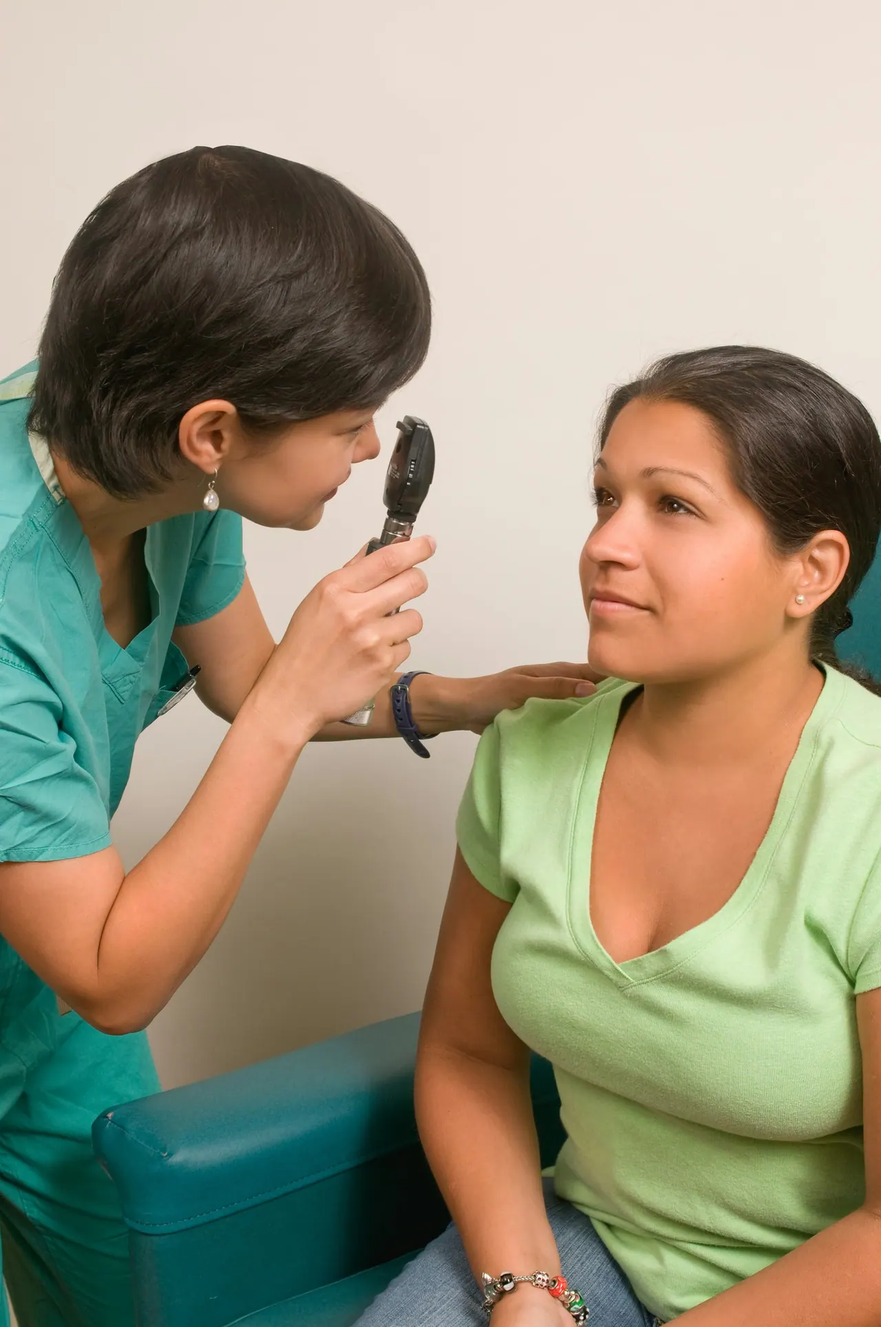 An optometrist checking a smiling woman’s eyes with a small light