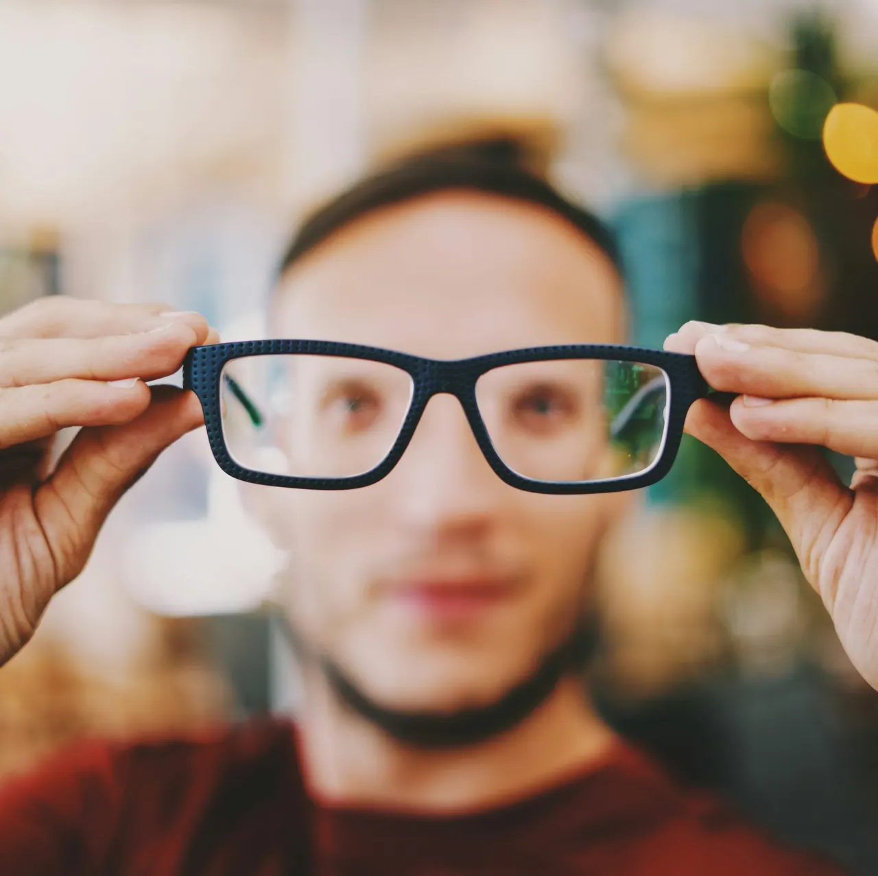 A pair of dark square glasses held up in front of a face