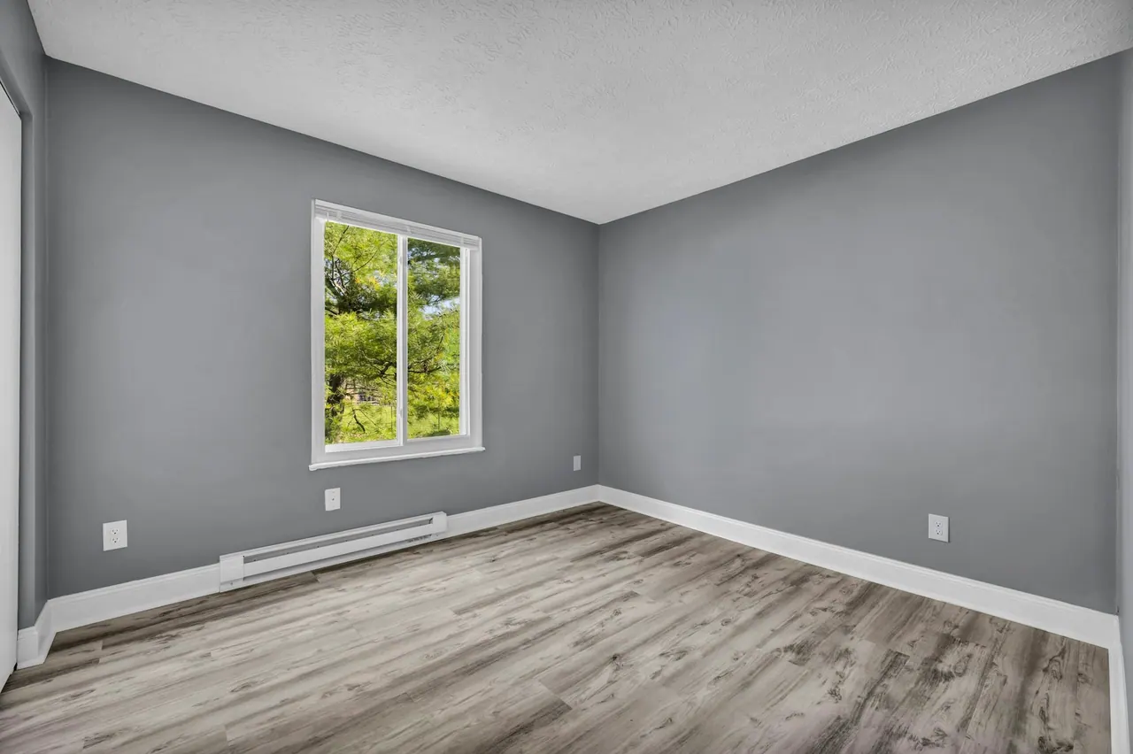 An empty room with painted walls, white trim, a window and a wood floor