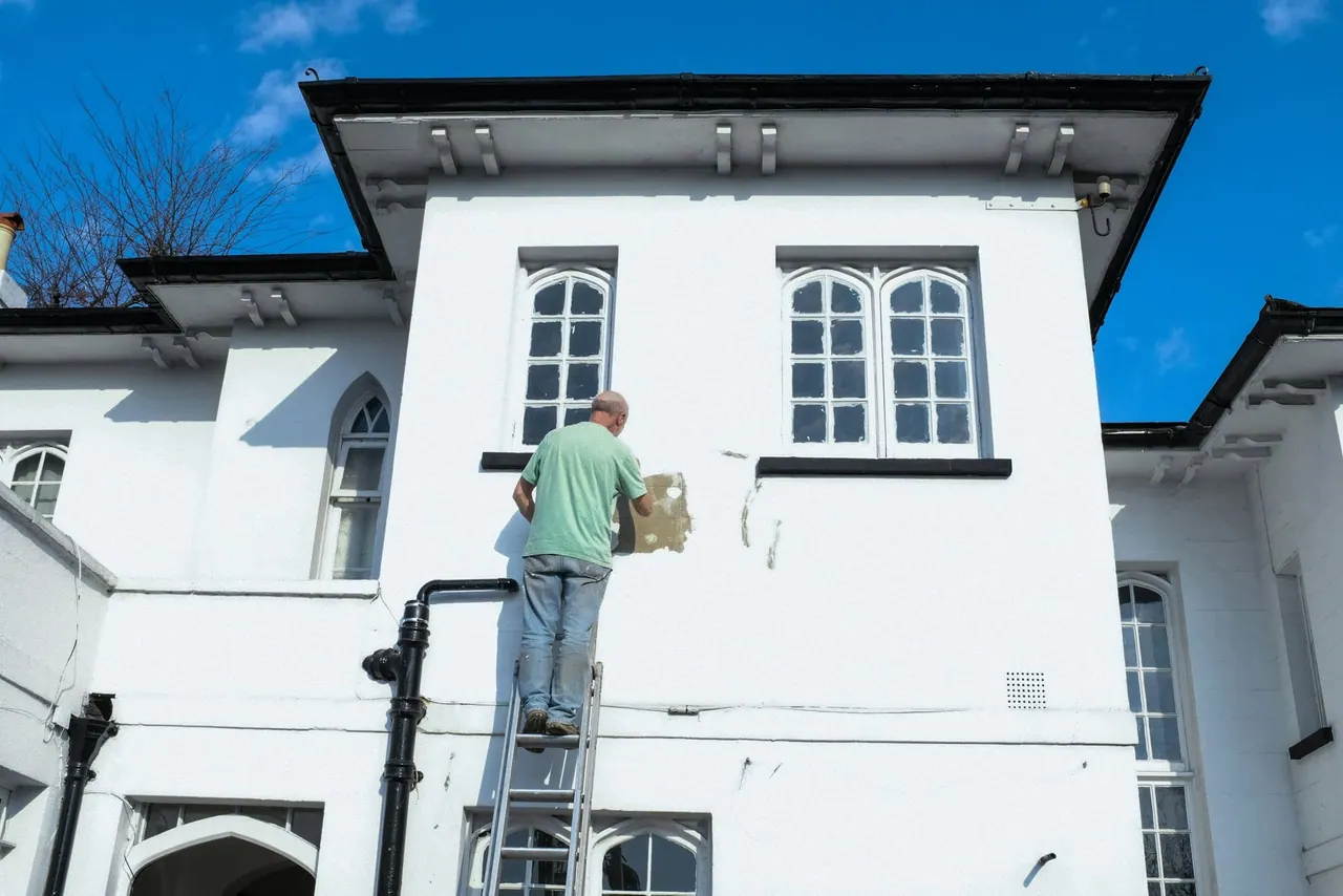 A painter on a ladder restoring the white facade of a two storey house