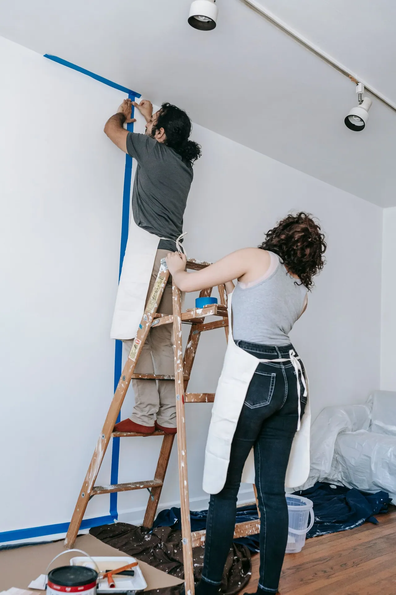 Two painters taping and preparing a white wall, one on a stepladder