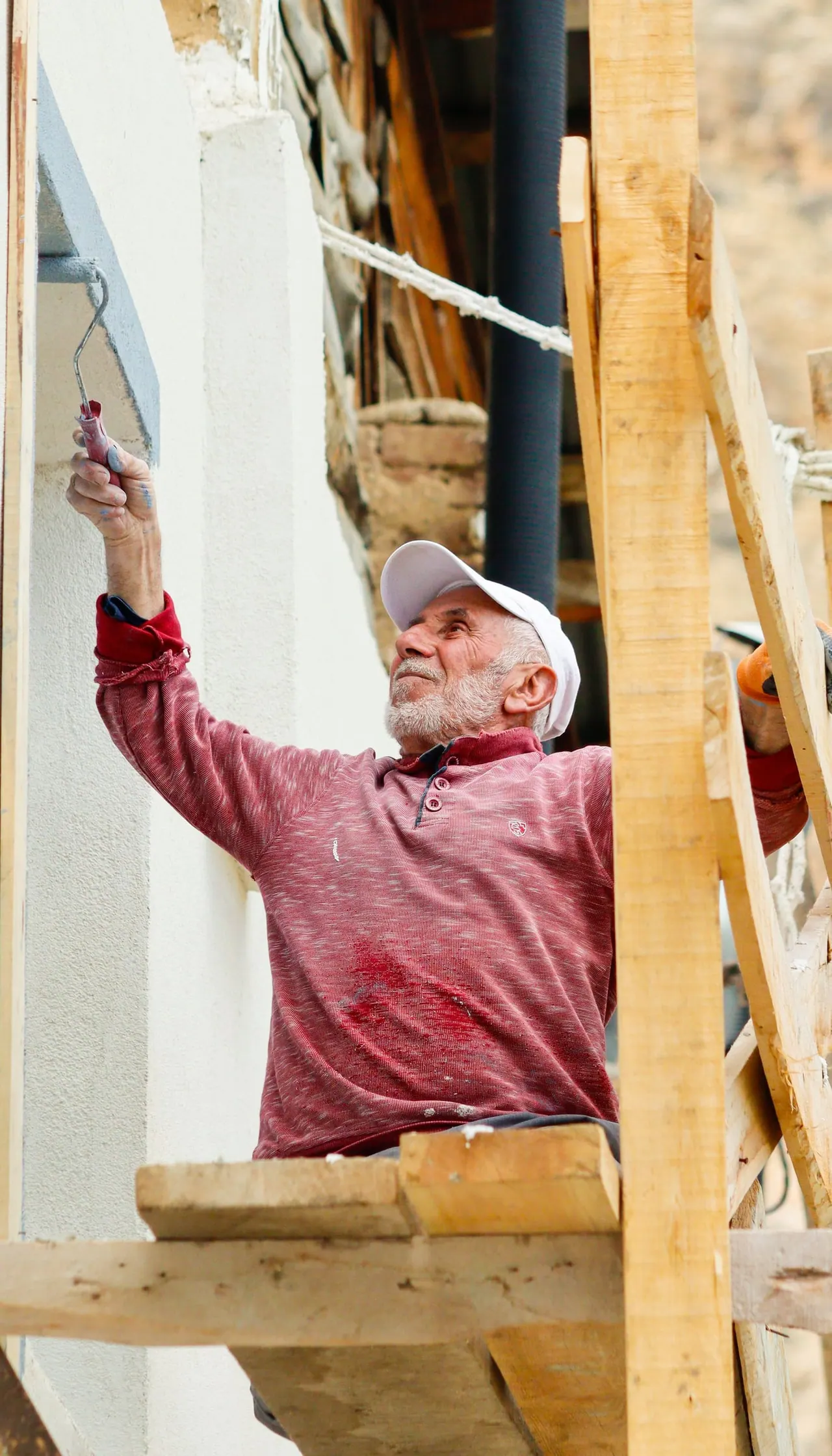 A senior painter on wooden scaffolding painting a white wall