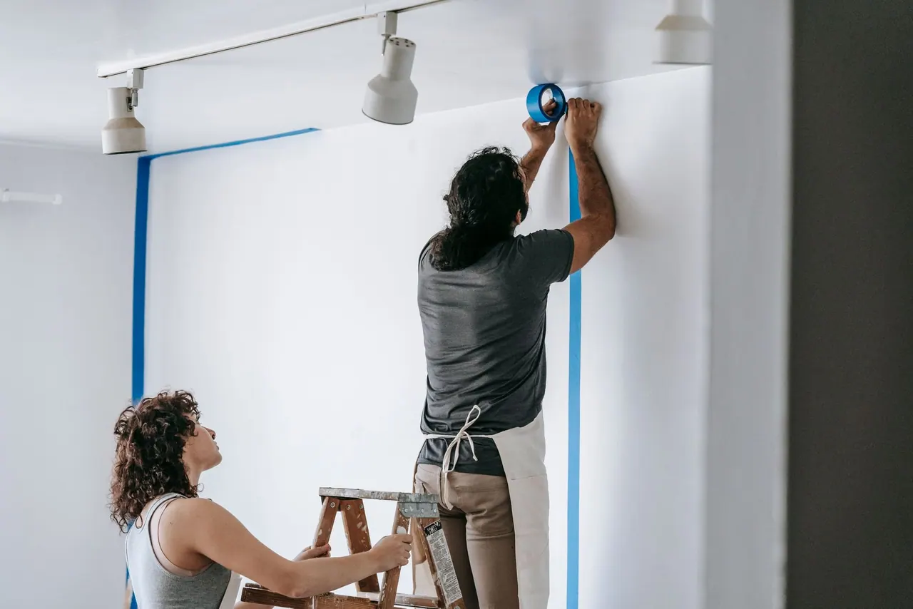Two of our pros taping a wall before painting, one on a stepladder