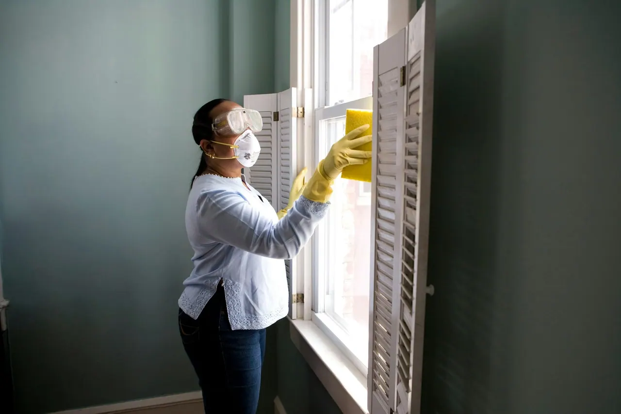 A technician in gloves, goggles and a mask treating a window frame