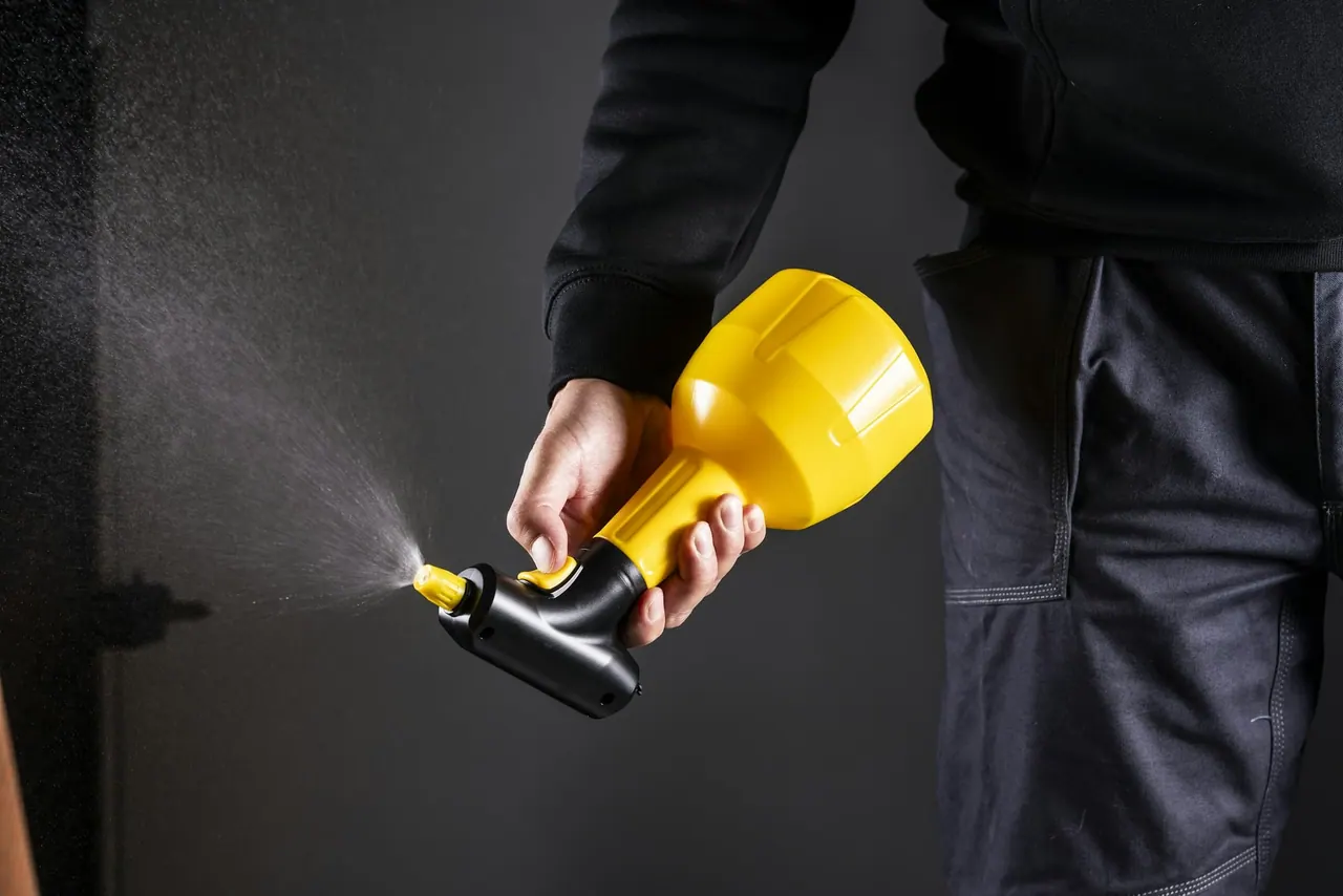 A gloved hand using a yellow hand sprayer