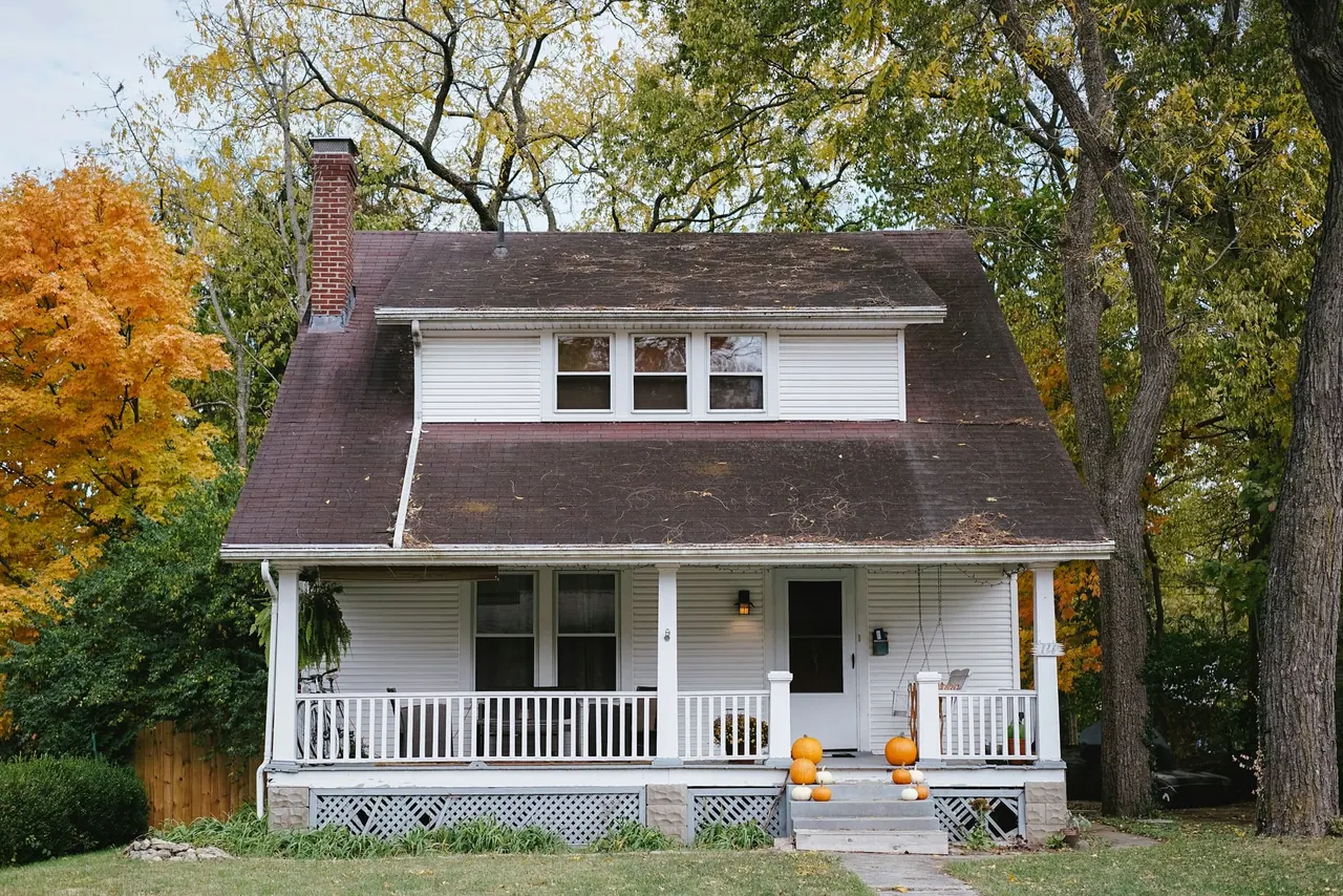 A white house with a deep porch among autumn trees