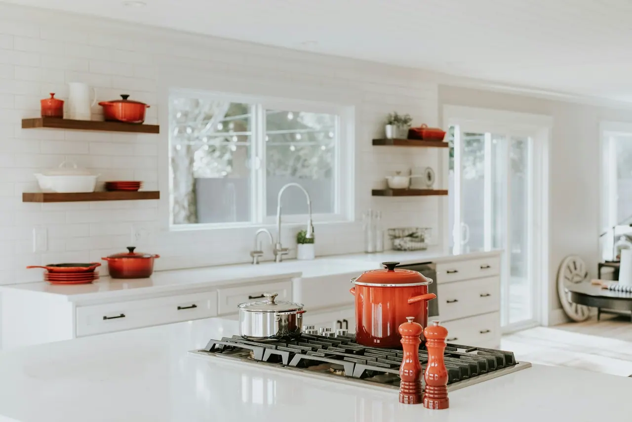 A bright, tidy kitchen with red pots on open shelves