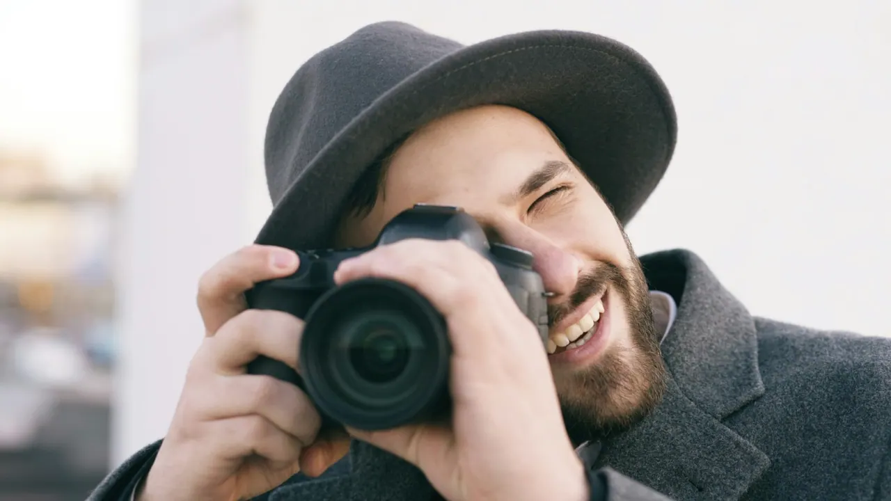 A smiling photographer in a grey hat and coat taking a picture