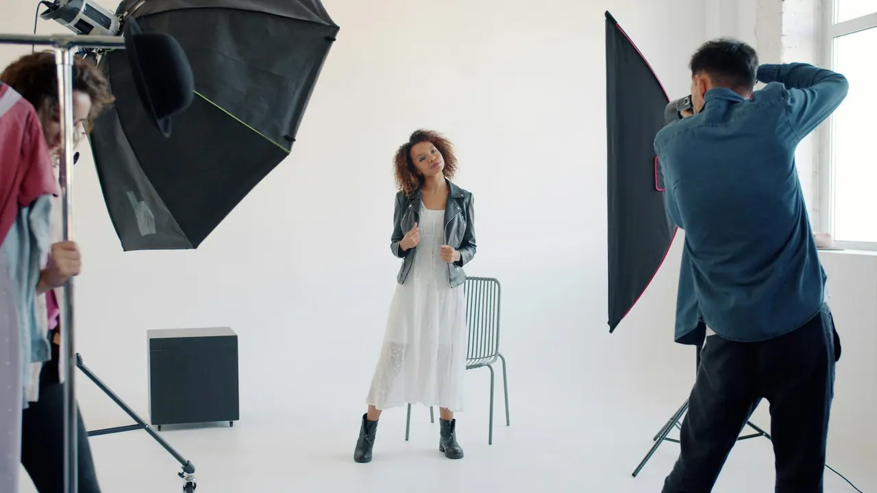A photographer shooting a model in a white dress and leather jacket in the studio