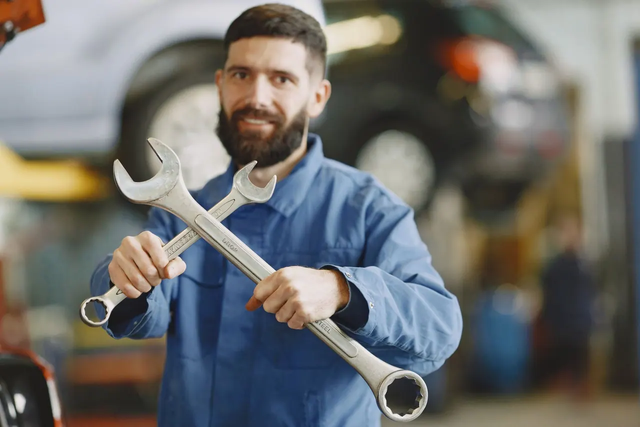 A smiling plumber in blue workwear holding two steel wrenches