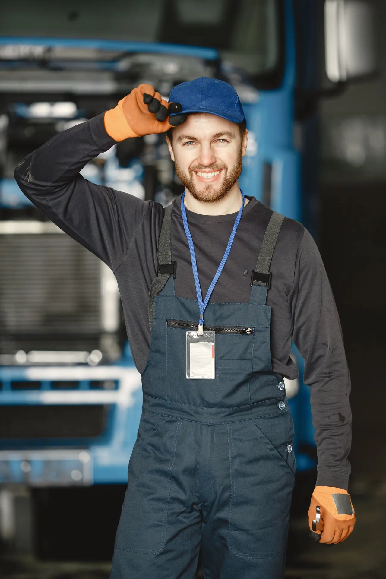 A smiling tradesman in overalls and a blue cap