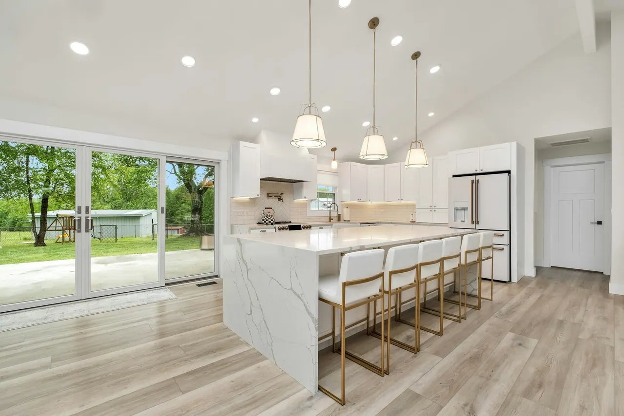 A bright kitchen with a marble island and pendant lights over the bar stools
