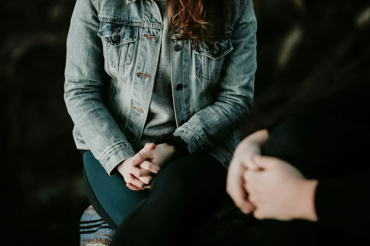 Two people sitting close together in a calm conversation, hands clasped