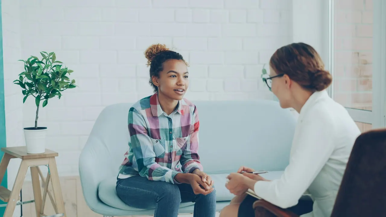 A smiling young woman talking with her psychologist on a pale blue sofa