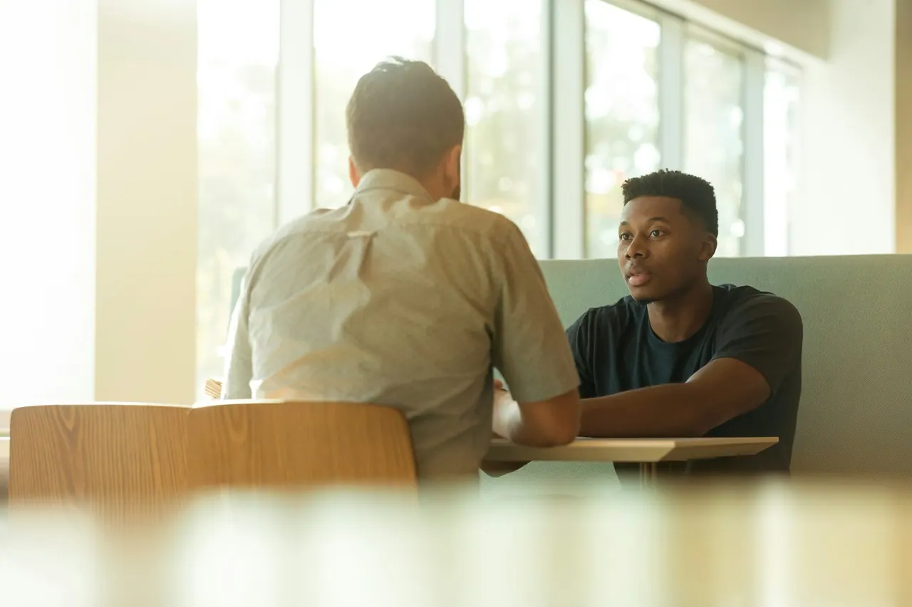 Two men talking warmly across a sunlit table