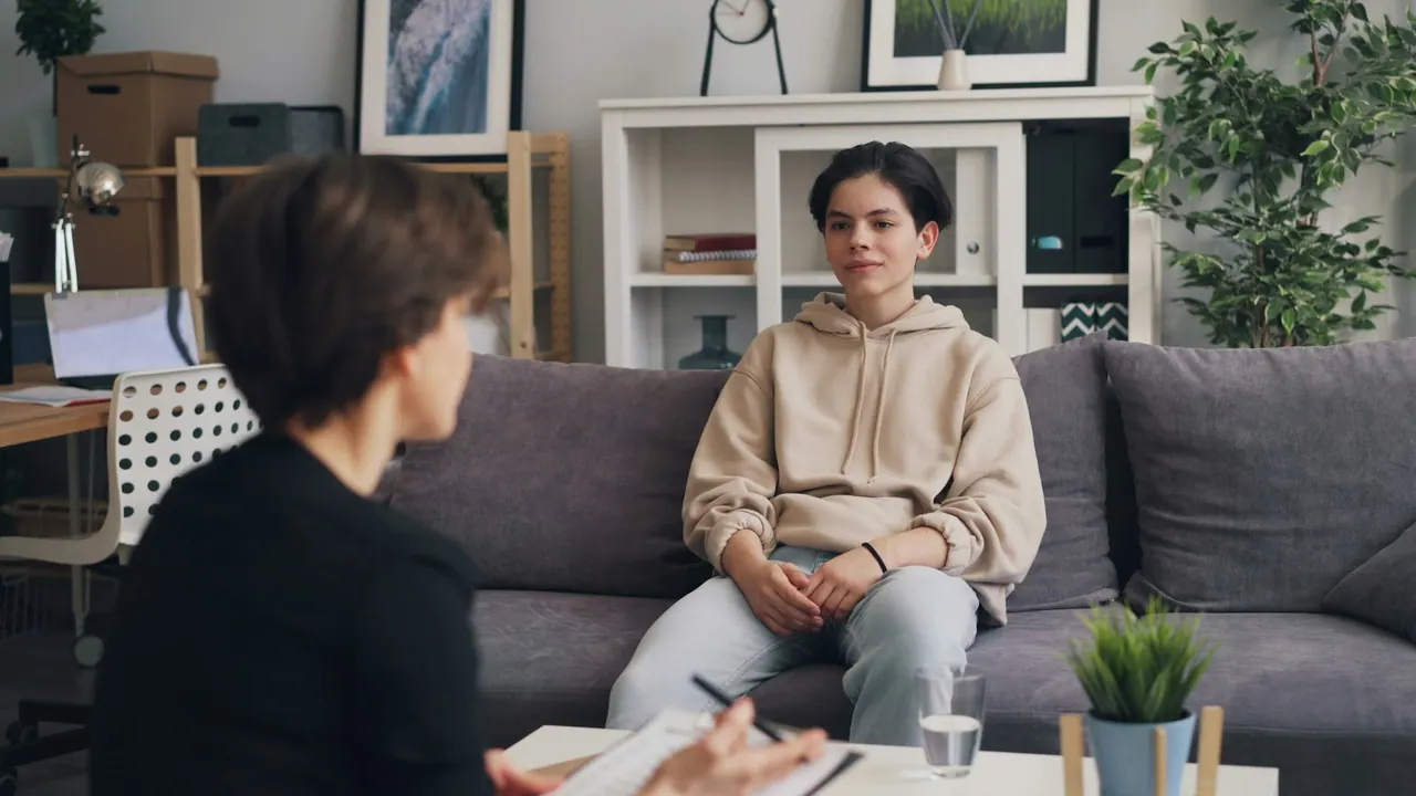 A teenager on a grey sofa talking with a counsellor
