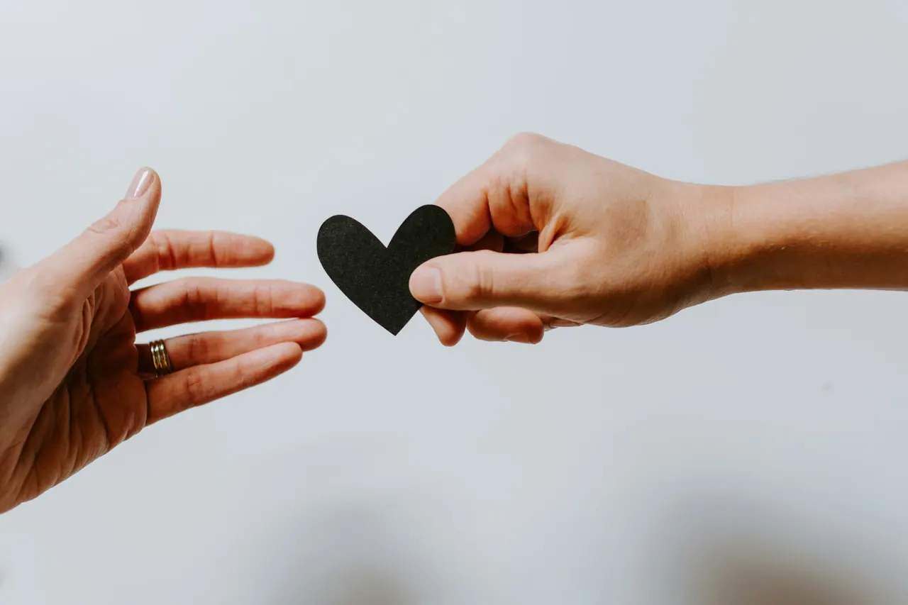 Two hands passing a small paper heart between them