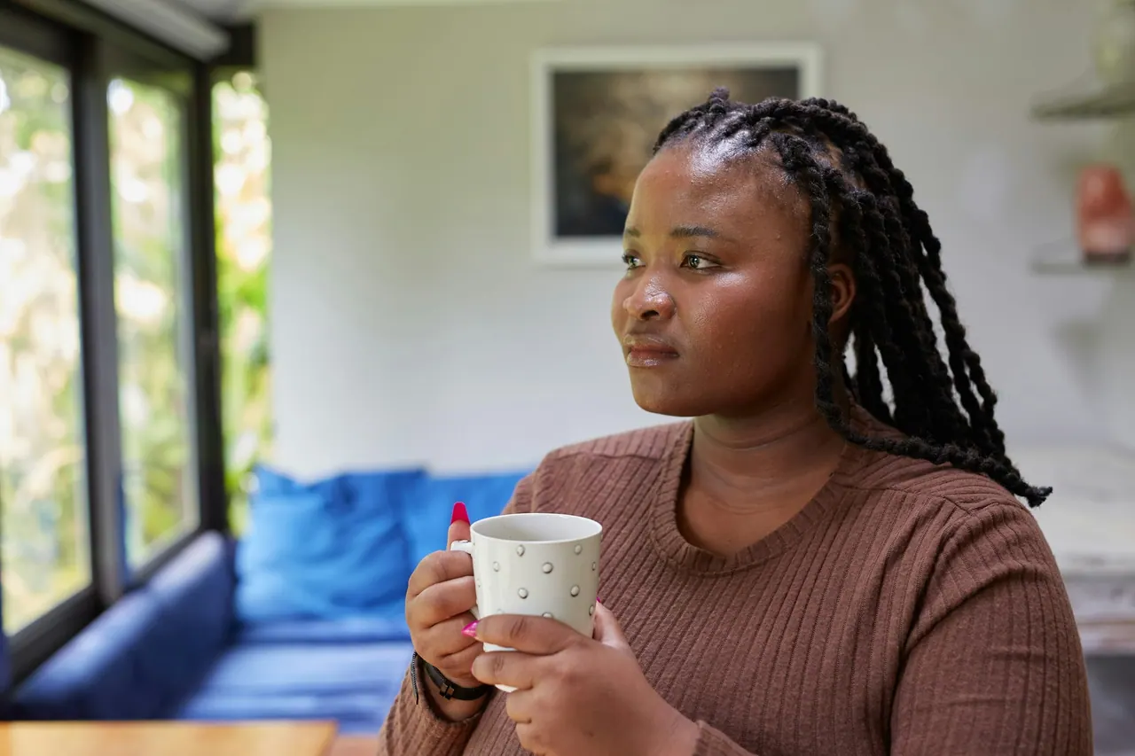 A woman holding a mug, looking out of a window, calm and thoughtful