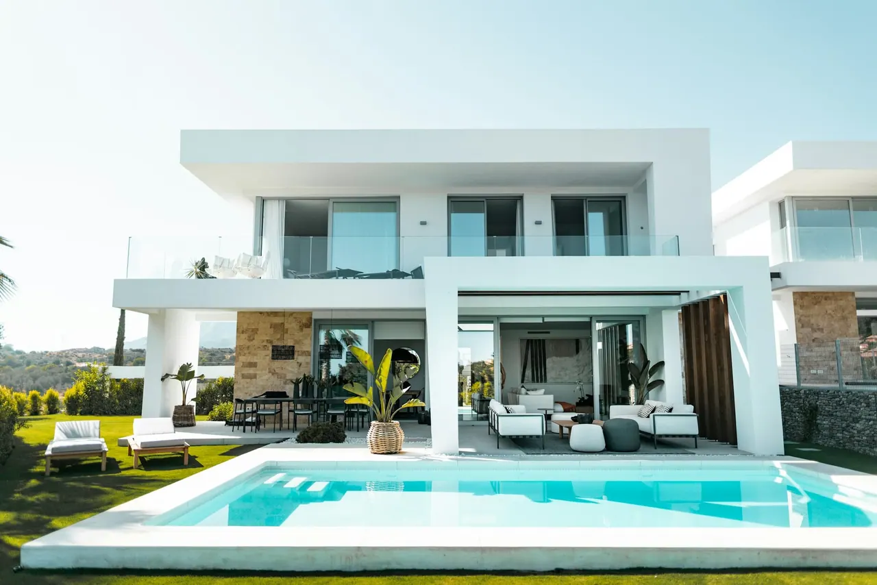 A white two storey villa with a pool and a shaded terrace