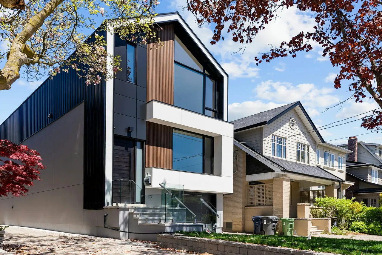 A narrow modern house with dark siding on a leafy street