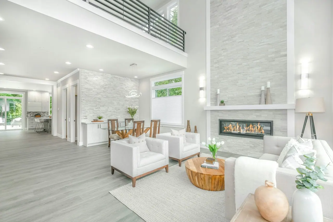 A bright living room with a stone fireplace wall and white armchairs