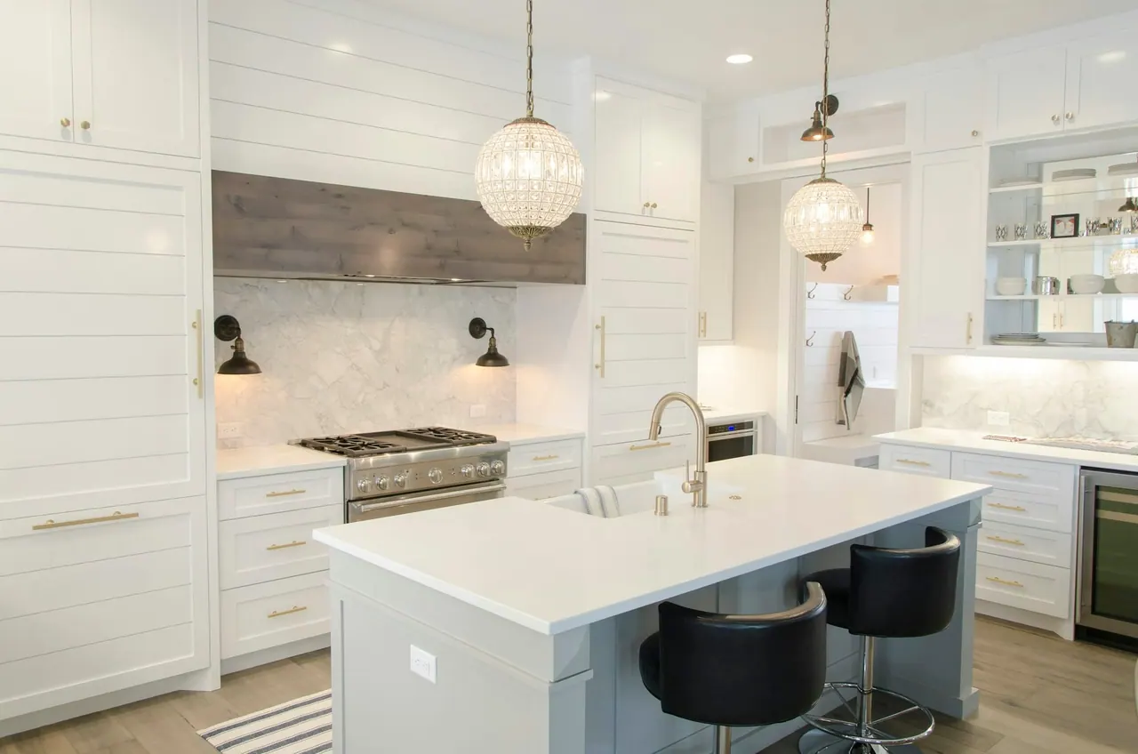 A white kitchen with a marble island and glass pendant lights