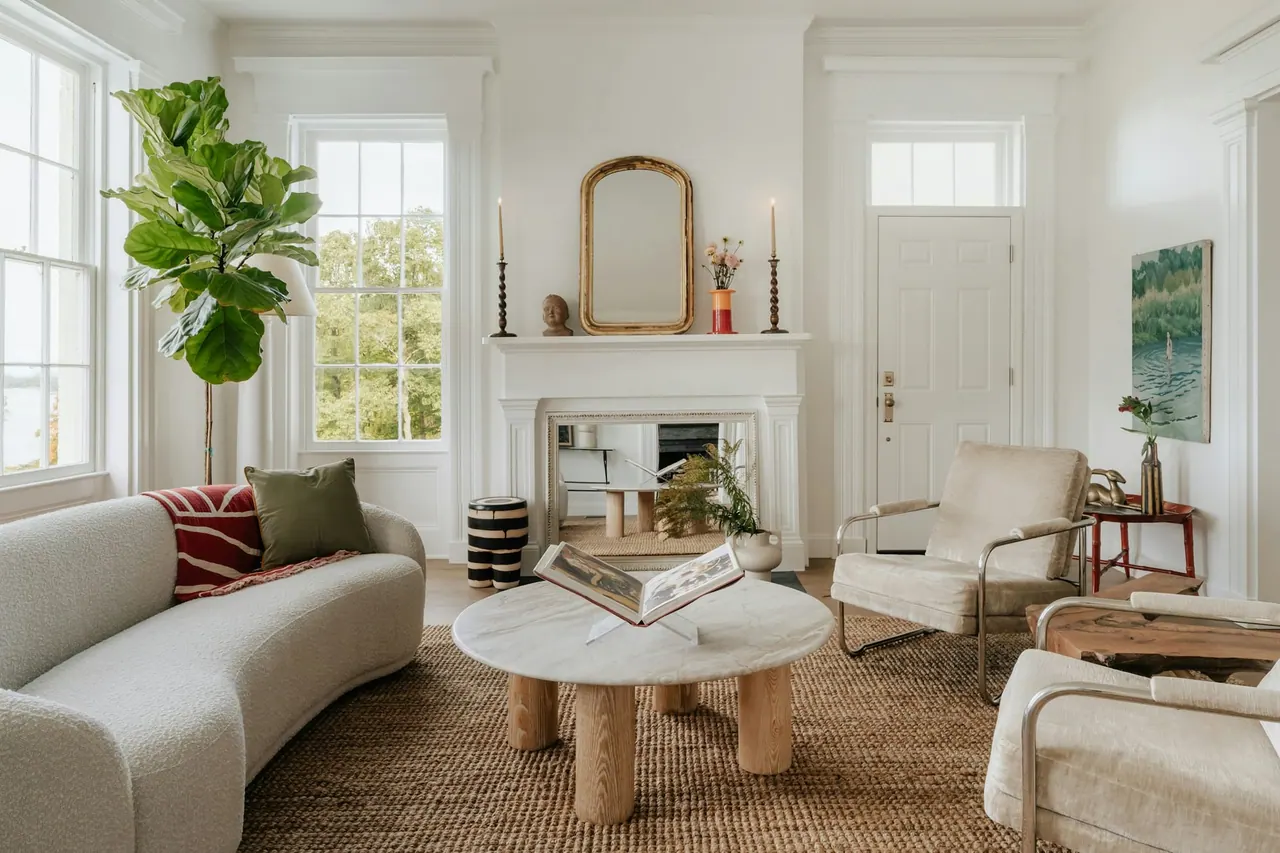 A calm living room with a curved sofa, a round stone table and a white fireplace