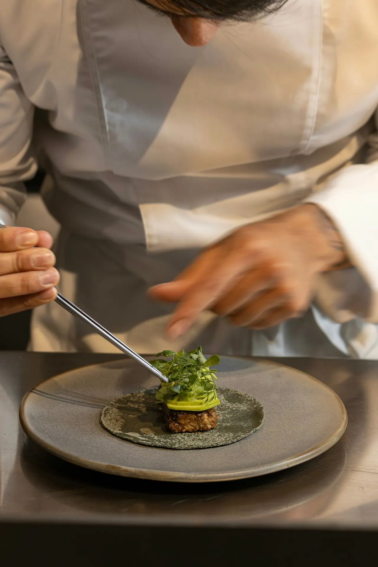 A chef finishing a small plated course with tweezers