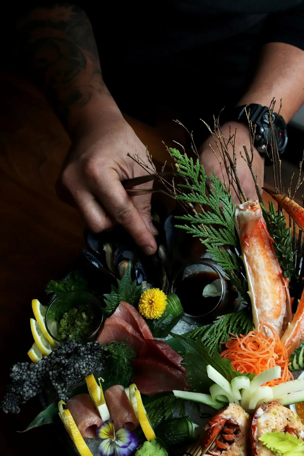 A chef garnishing a seafood platter with flowers and herbs