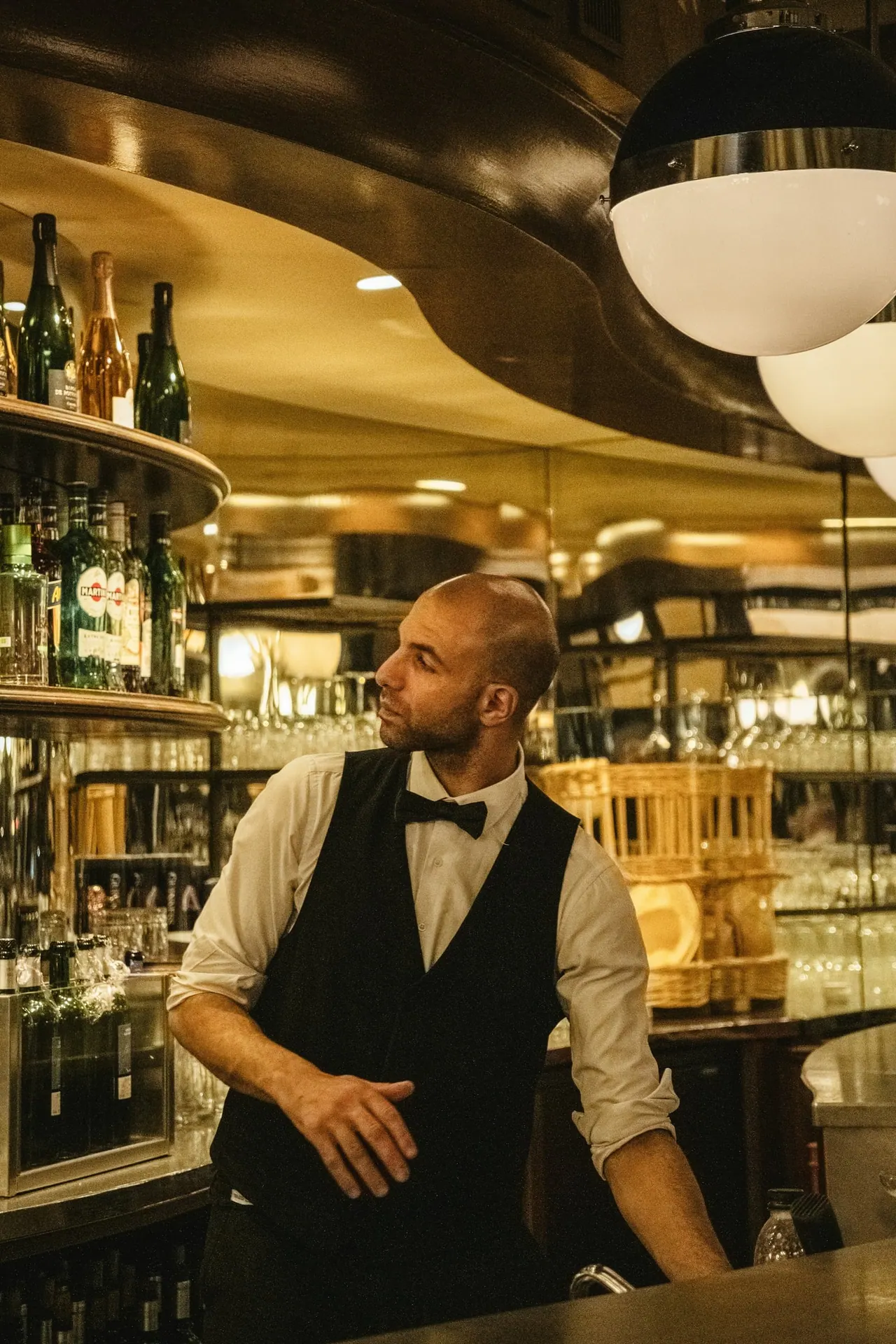 Our bar host in a waistcoat and bow tie behind a warmly lit bar
