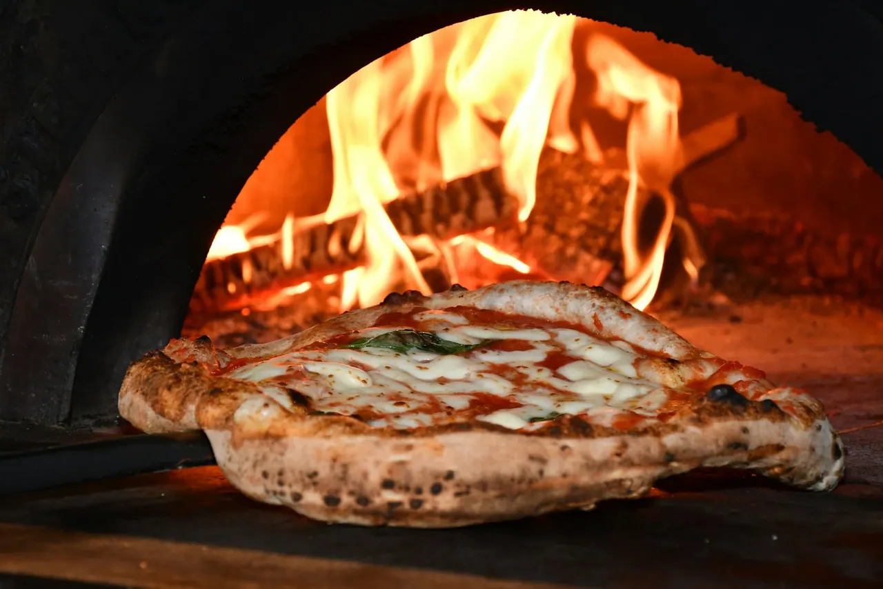 A pizza blistering in a wood fired oven, flames behind it