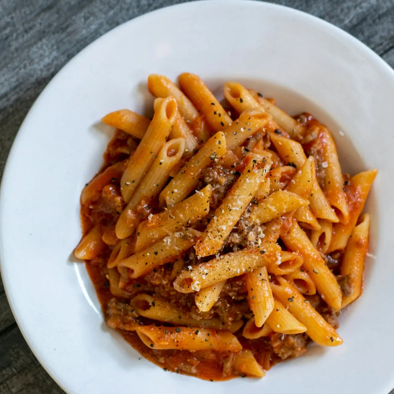 A bowl of penne in a rich tomato sauce, packed to go