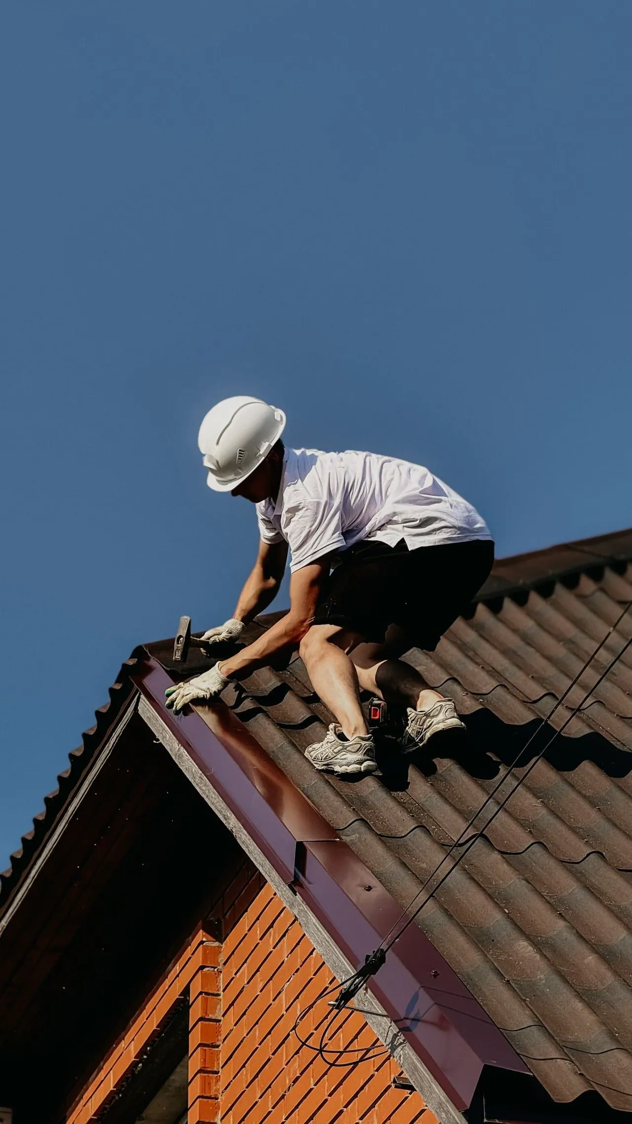 A roofer in a white helmet fixing a roof against a deep blue sky