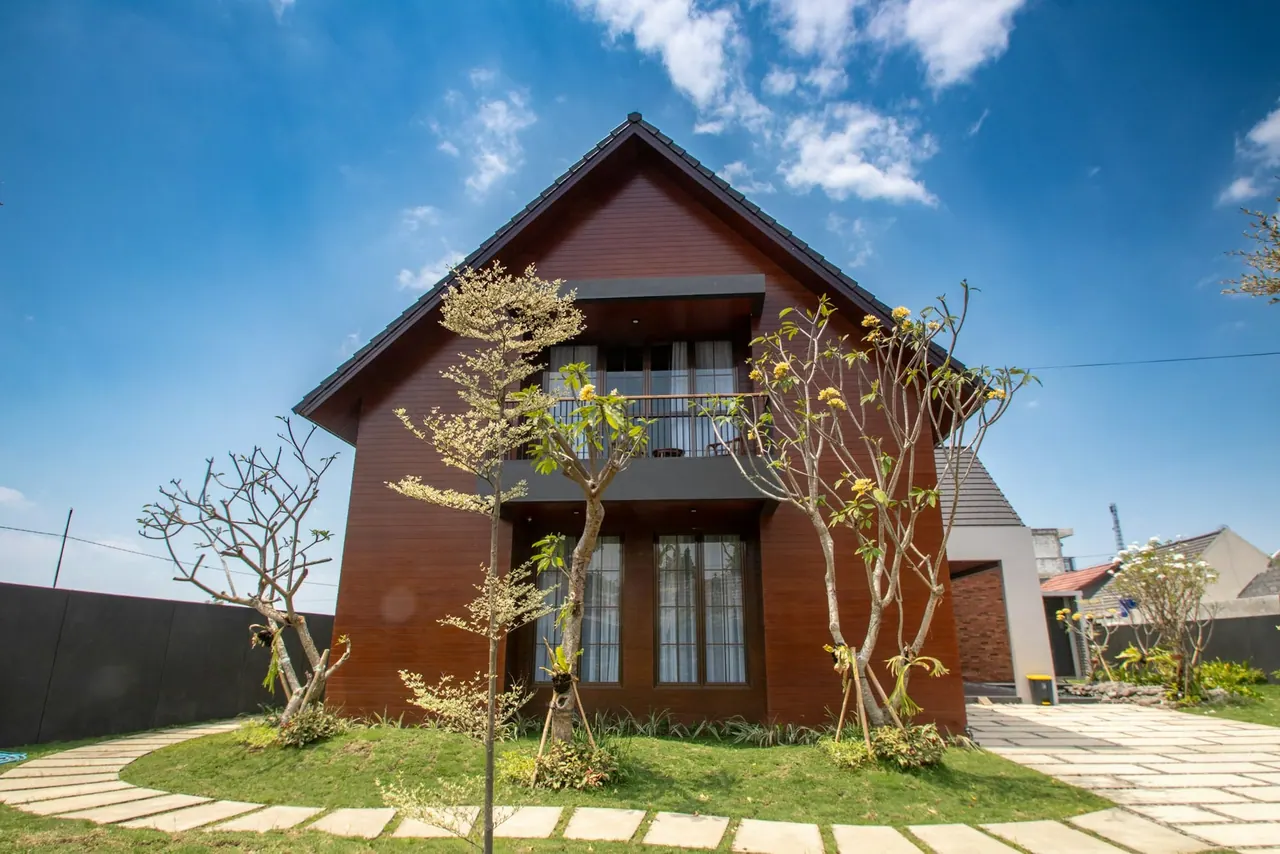 A two storey wooden house with a pitched roof and young trees in the front garden