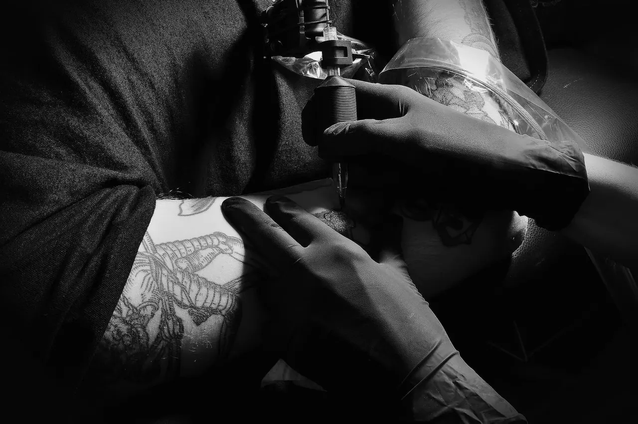 Gloved hands at work on a tattoo, in black and white