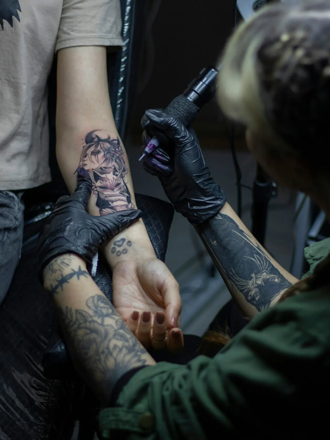 A gloved artist working on a black and grey forearm piece