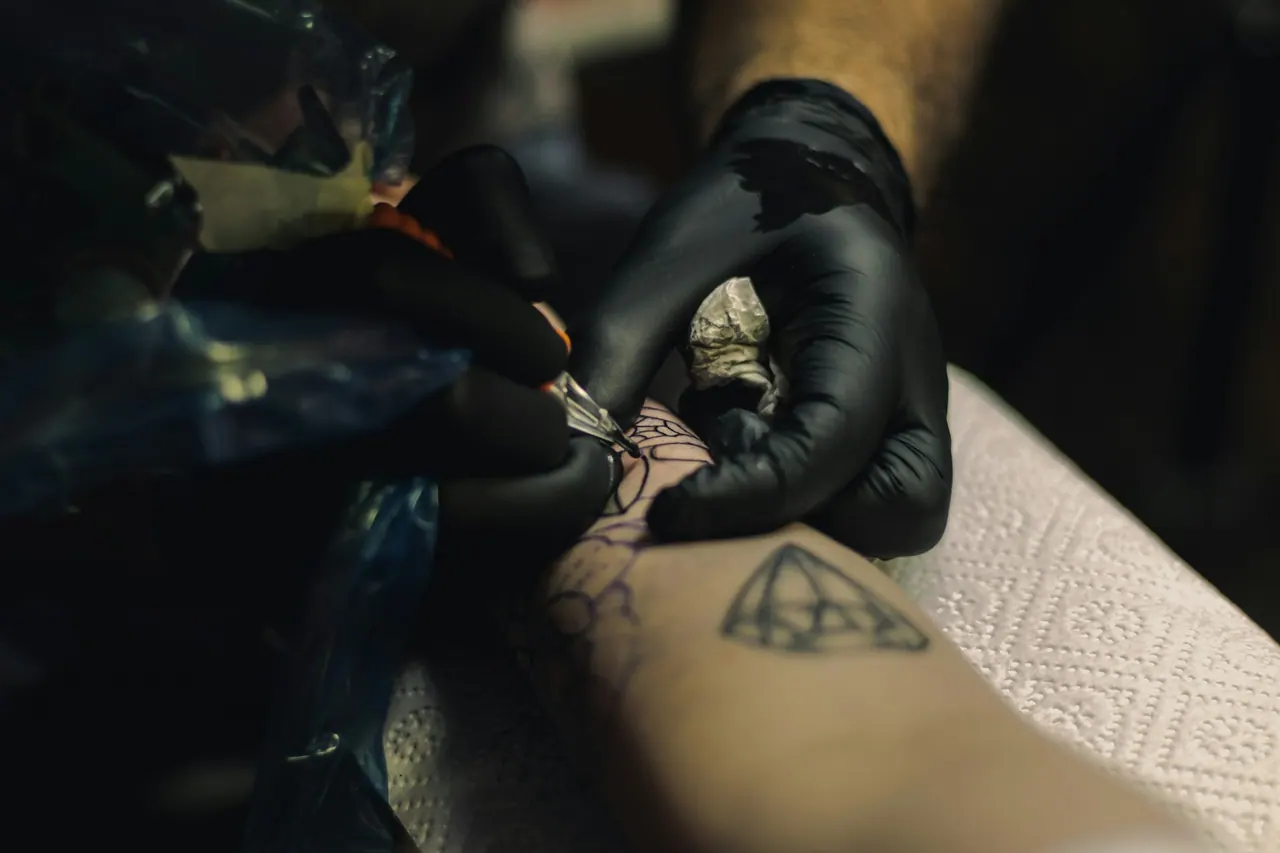 An artist in black gloves drawing a fine line tattoo