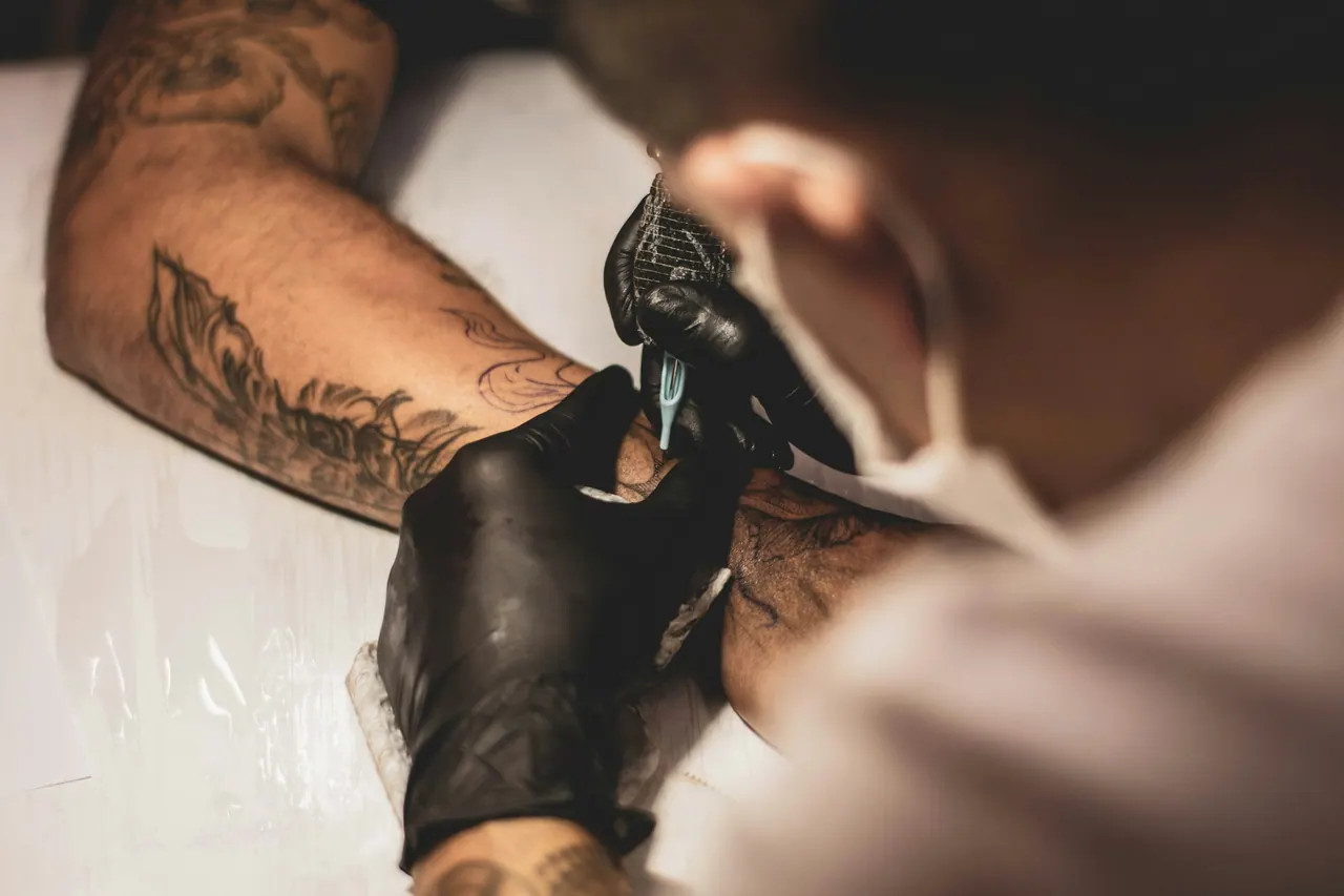 An artist in black gloves tattooing a forearm