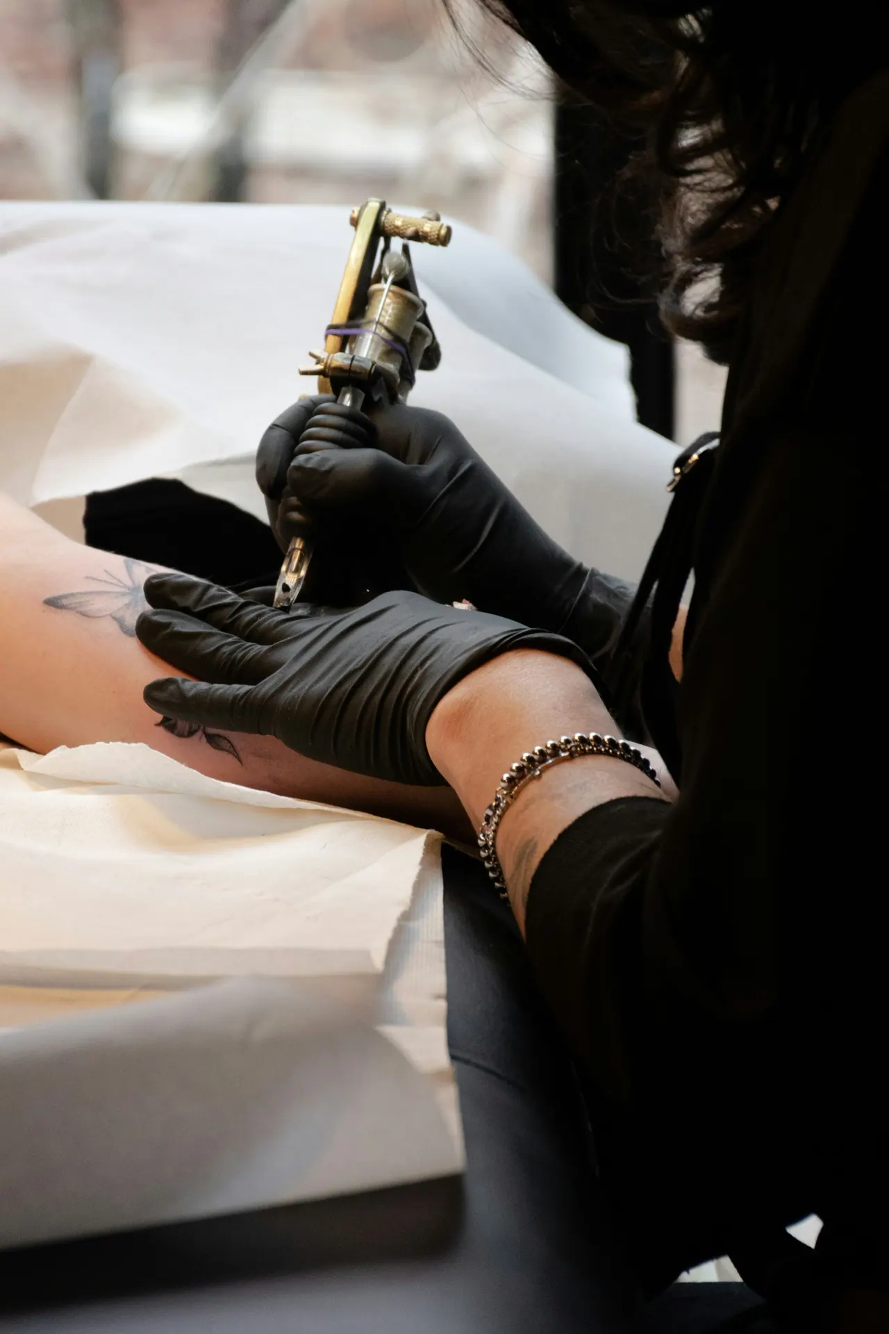 An artist in black gloves holding a brass coil machine over a forearm