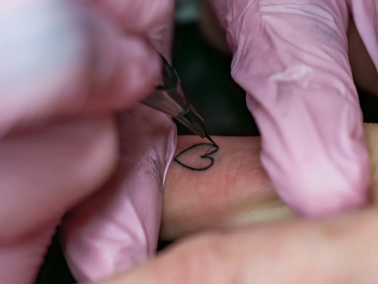 A tiny fine line heart tattooed on a finger