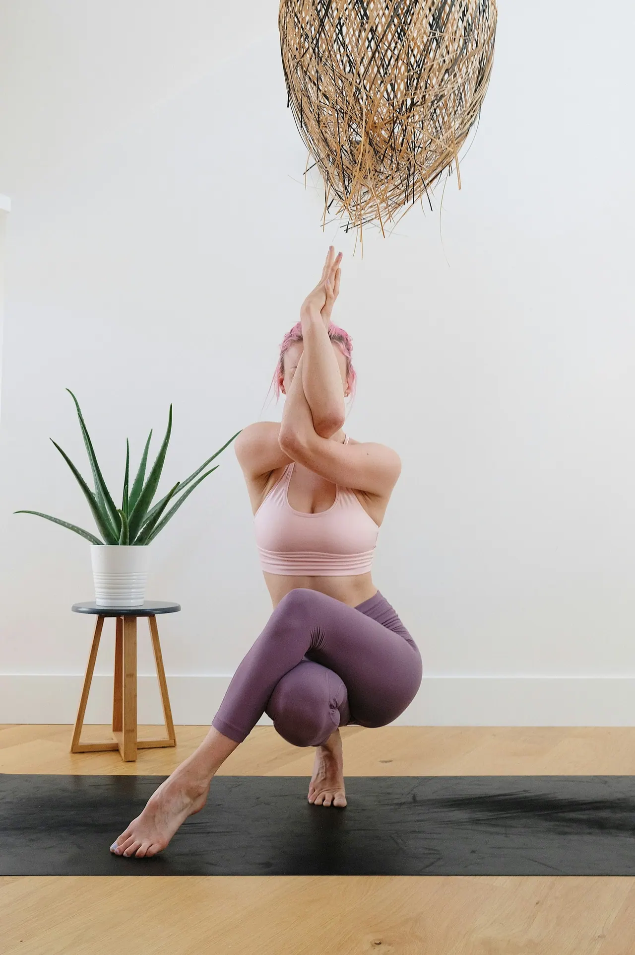 A woman balancing in eagle pose in a bright white room