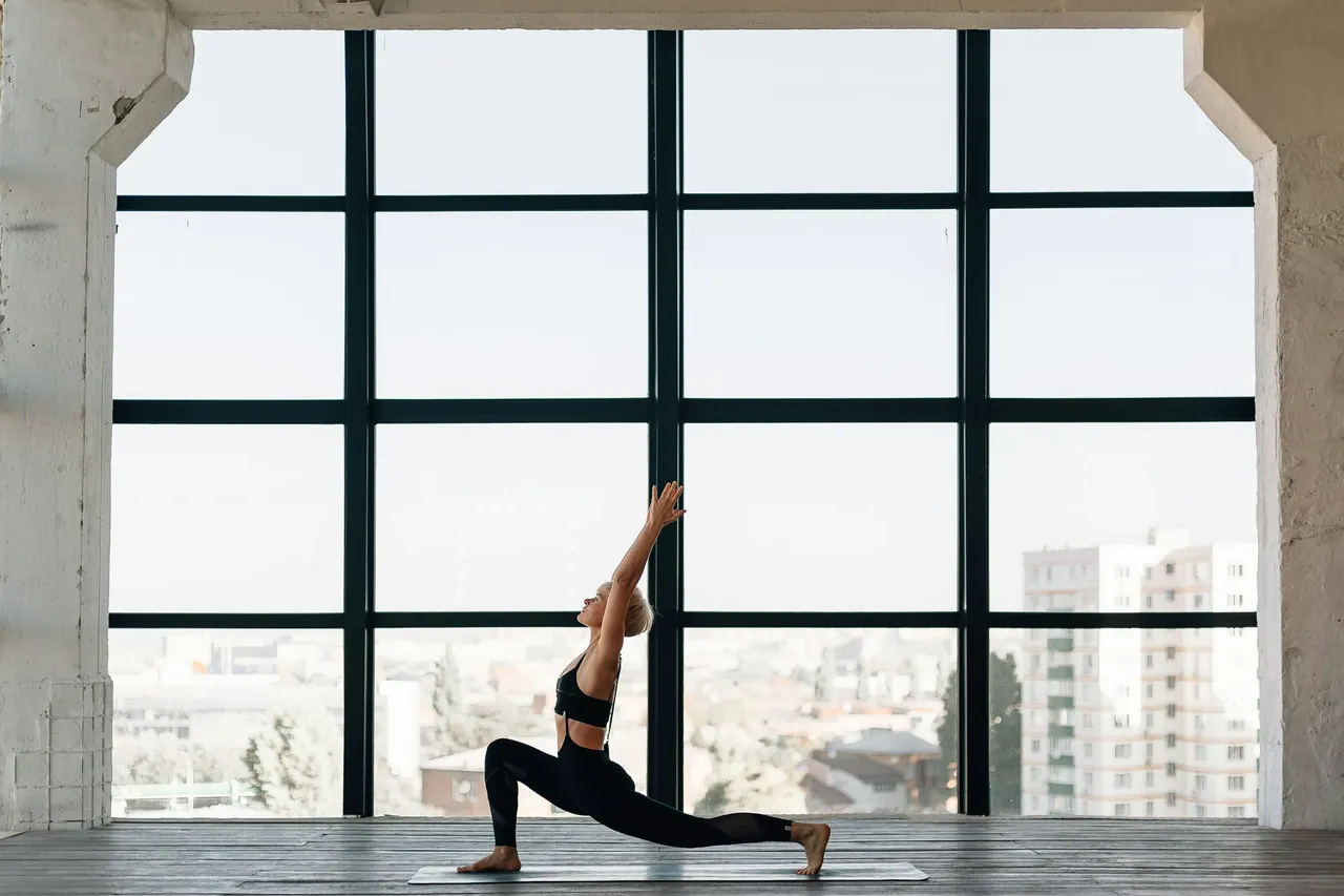 A low lunge with arms raised by a tall industrial window