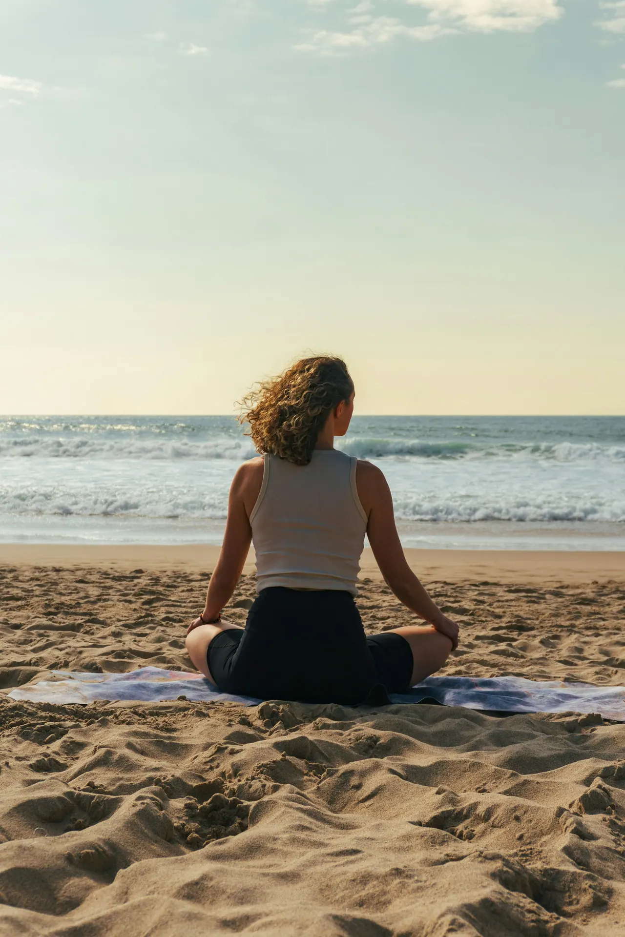 A woman meditating on the sand at sunrise, facing the sea