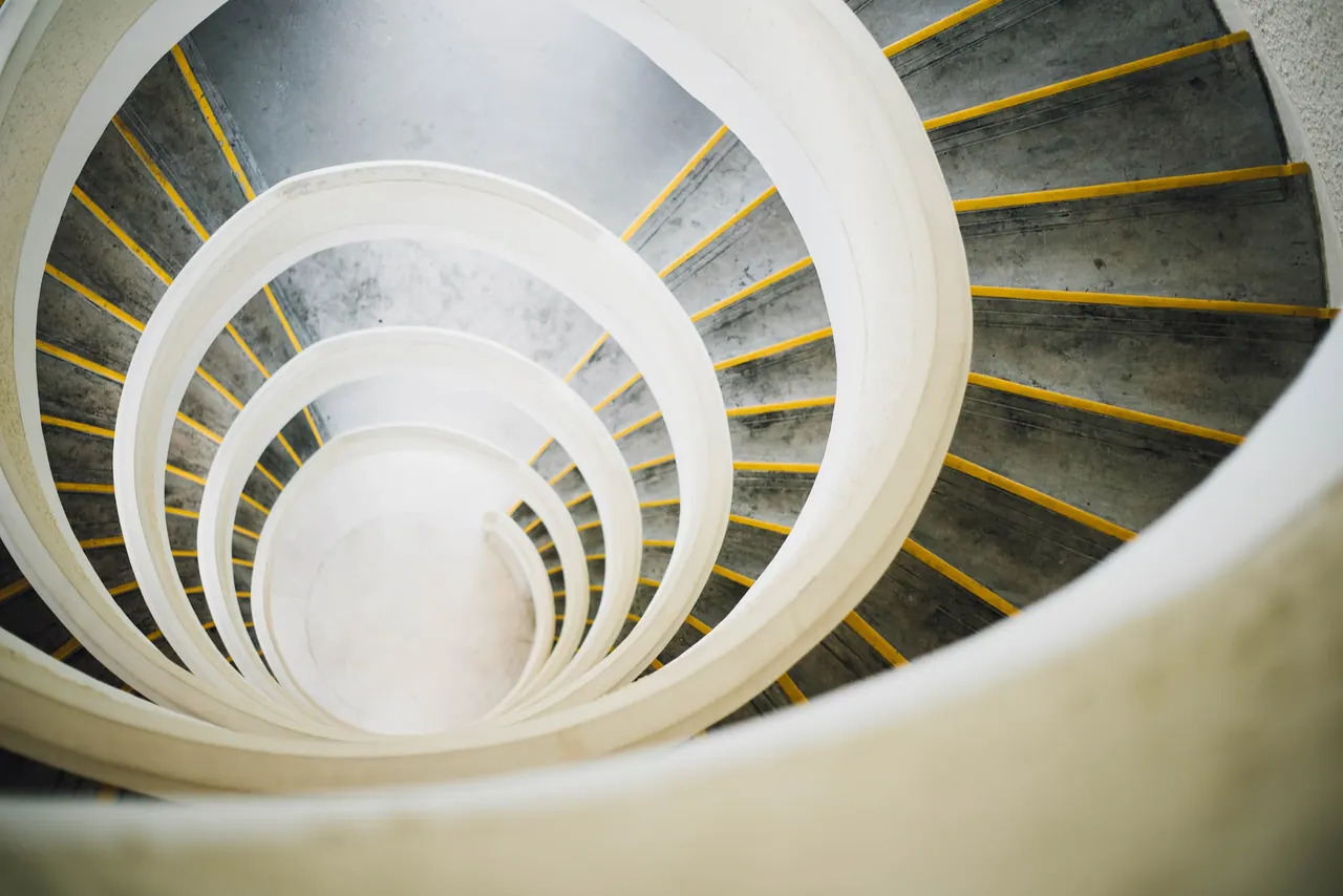 Looking down a white spiral staircase that rises floor after floor.