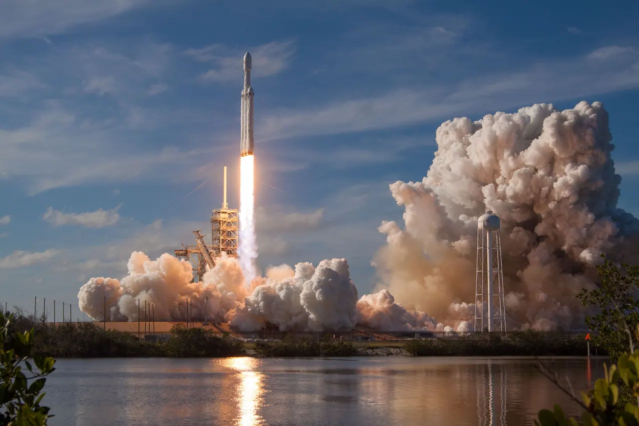 A rocket climbing through a deep blue sky, trailing flame and smoke.